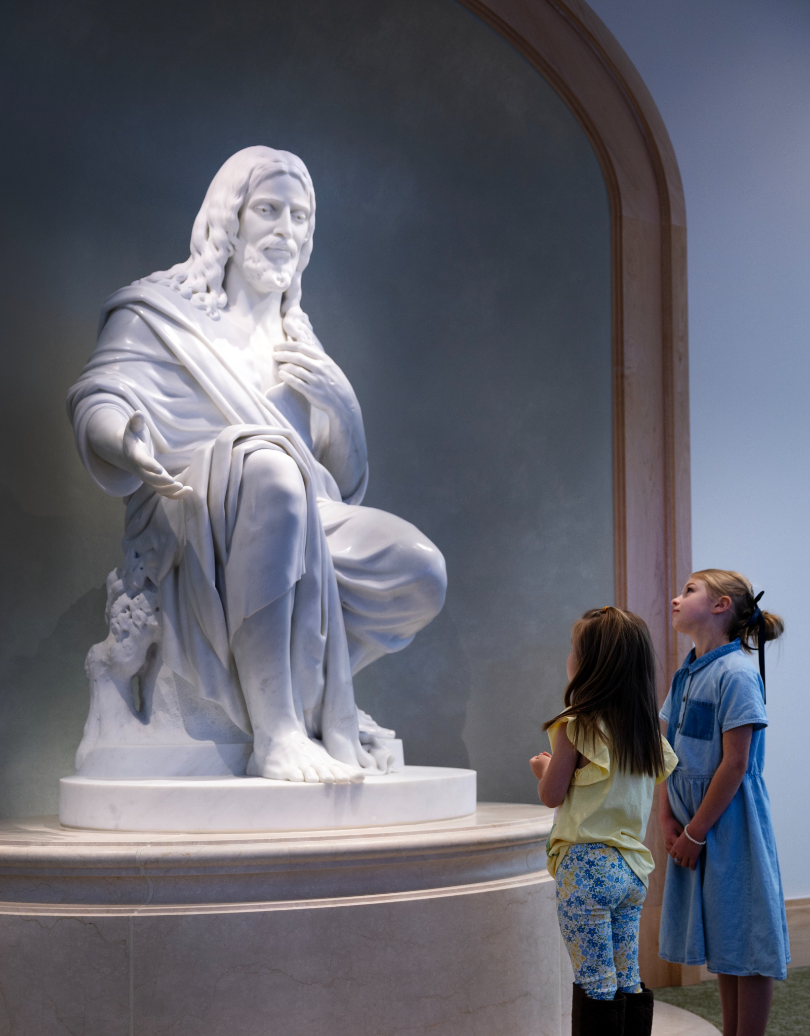Two girls look up at the marble Christus statue