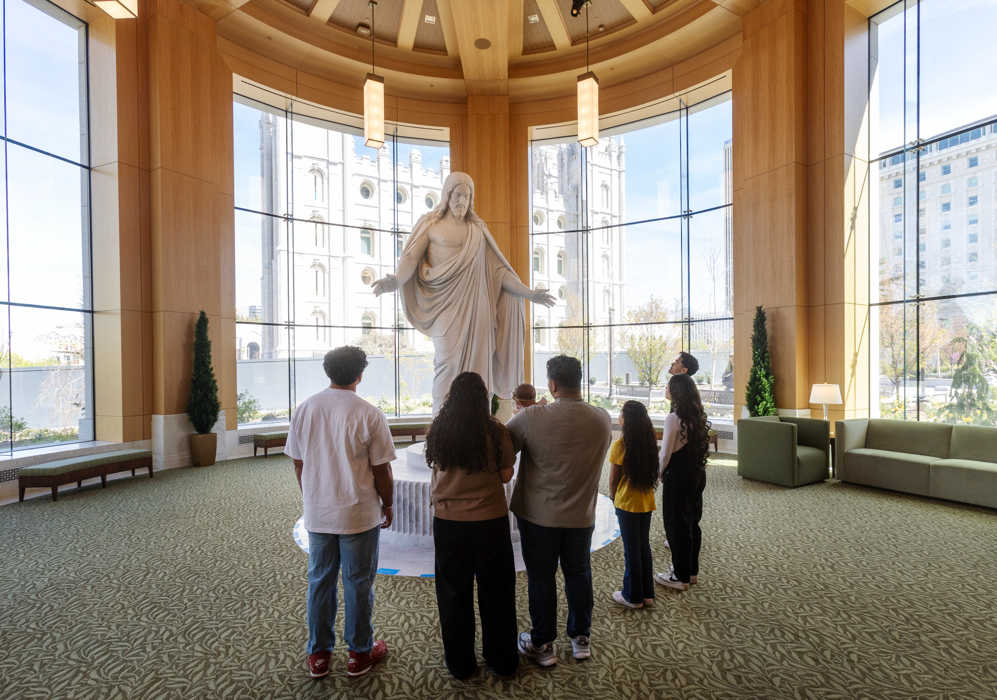 Family viewing the Christus statue with the Salt Lake Temple visible through windows behind
